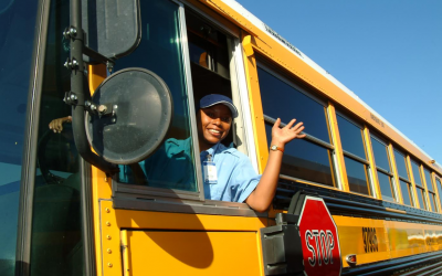 a bus driver waving out of the driver window of a school bus